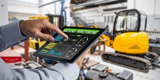 Hands holding a tablet computer with a heavy equipment machine in the background